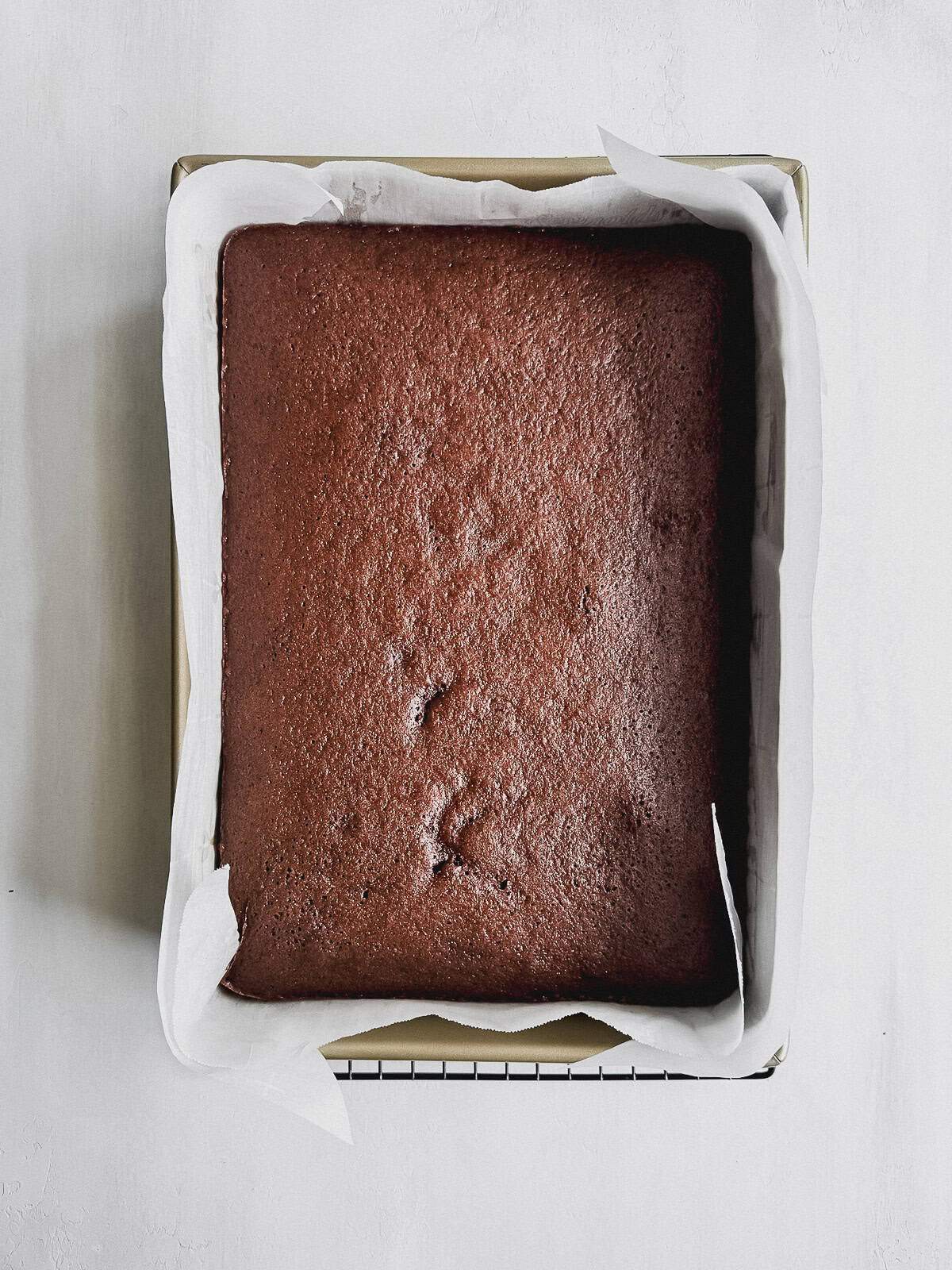 Baked Texas sheet cake in a cake pan on a wire rack.