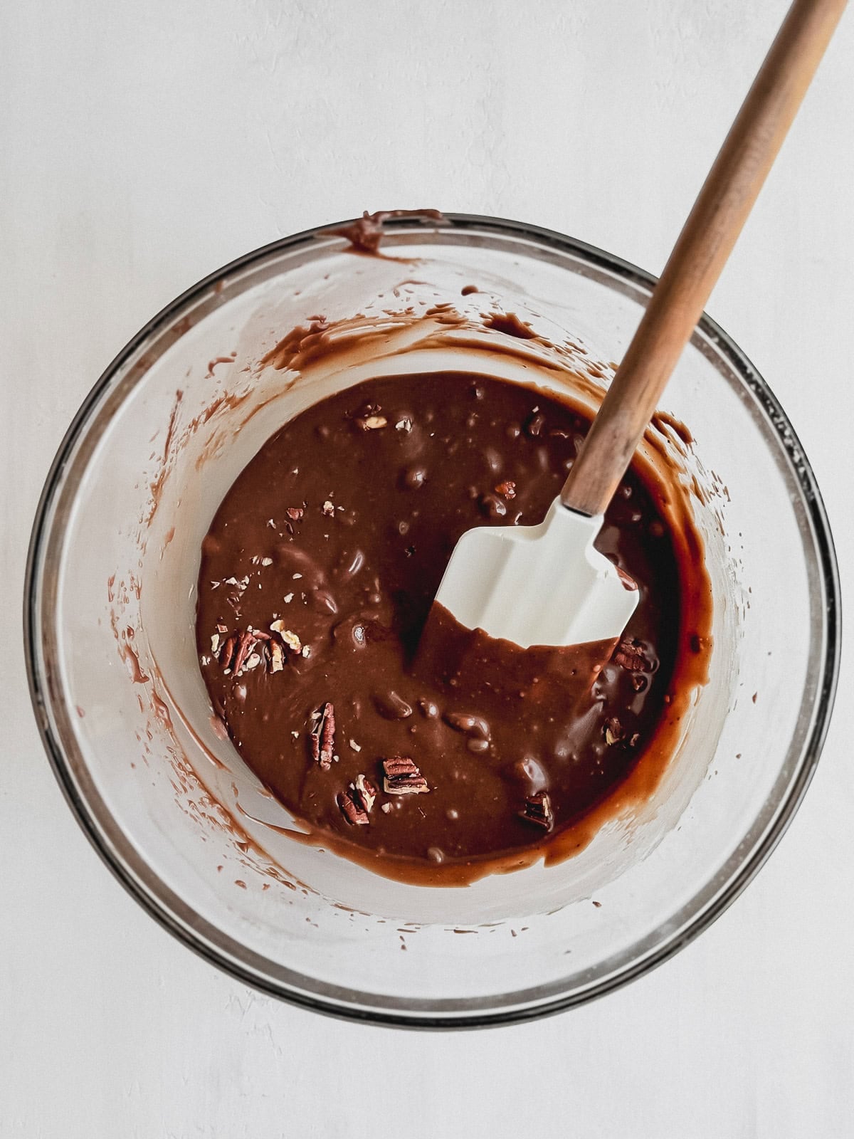 Fudge frosting and chopped pecans in a large mixing bowl with a rubber spatula.