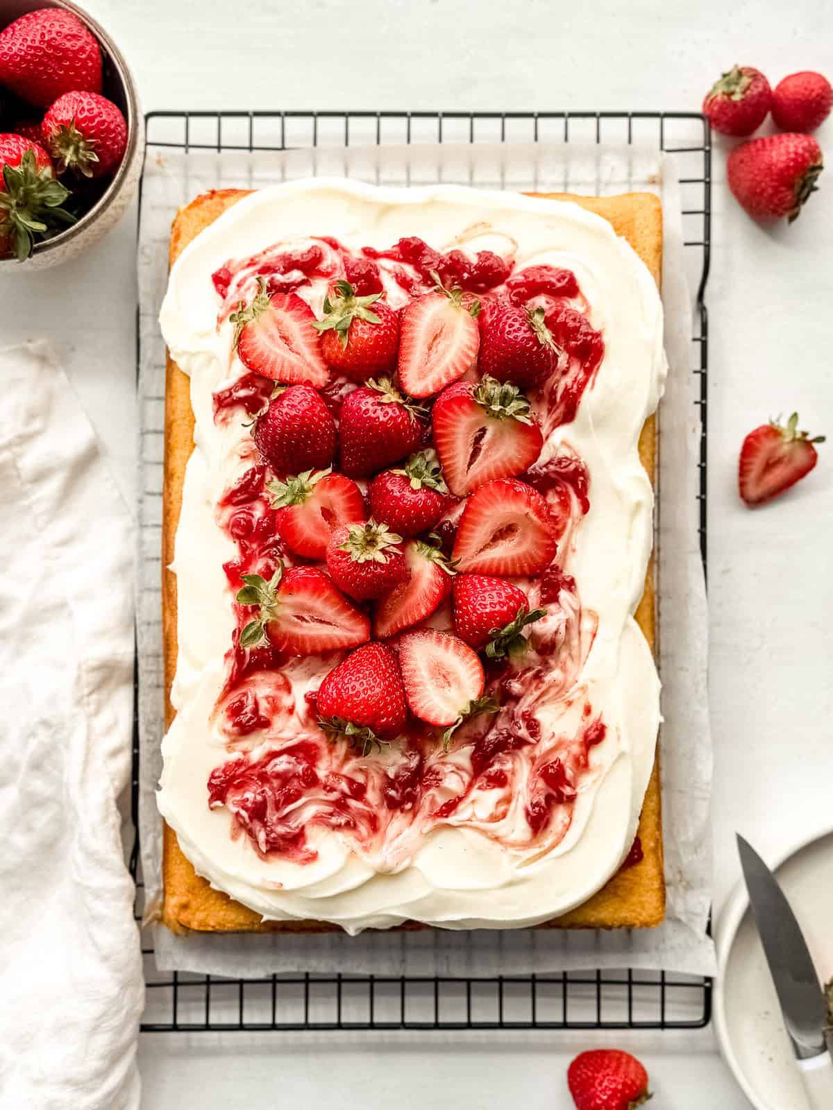 Vanilla cake with strawberry filling topped with cream cheese frosting and fresh strawberries on a wire rack.