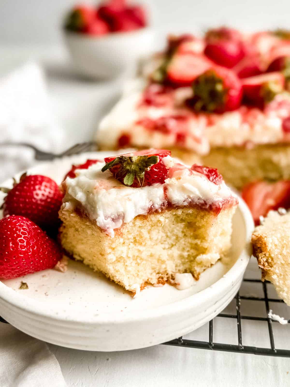 A slice of vanilla cake with strawberry filling with a piece missing on a dessert plate.