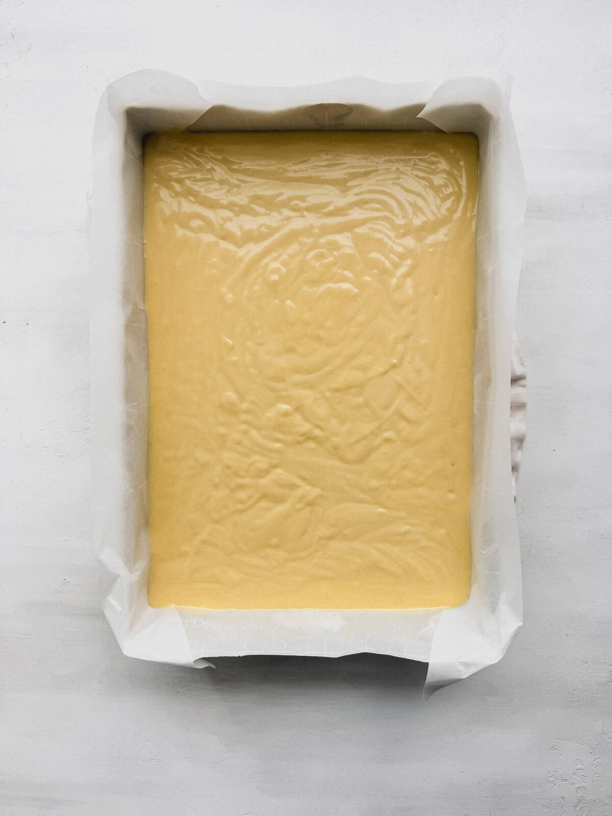 Vanilla cake batter in a 9x13 cake pan lined with parchment paper.