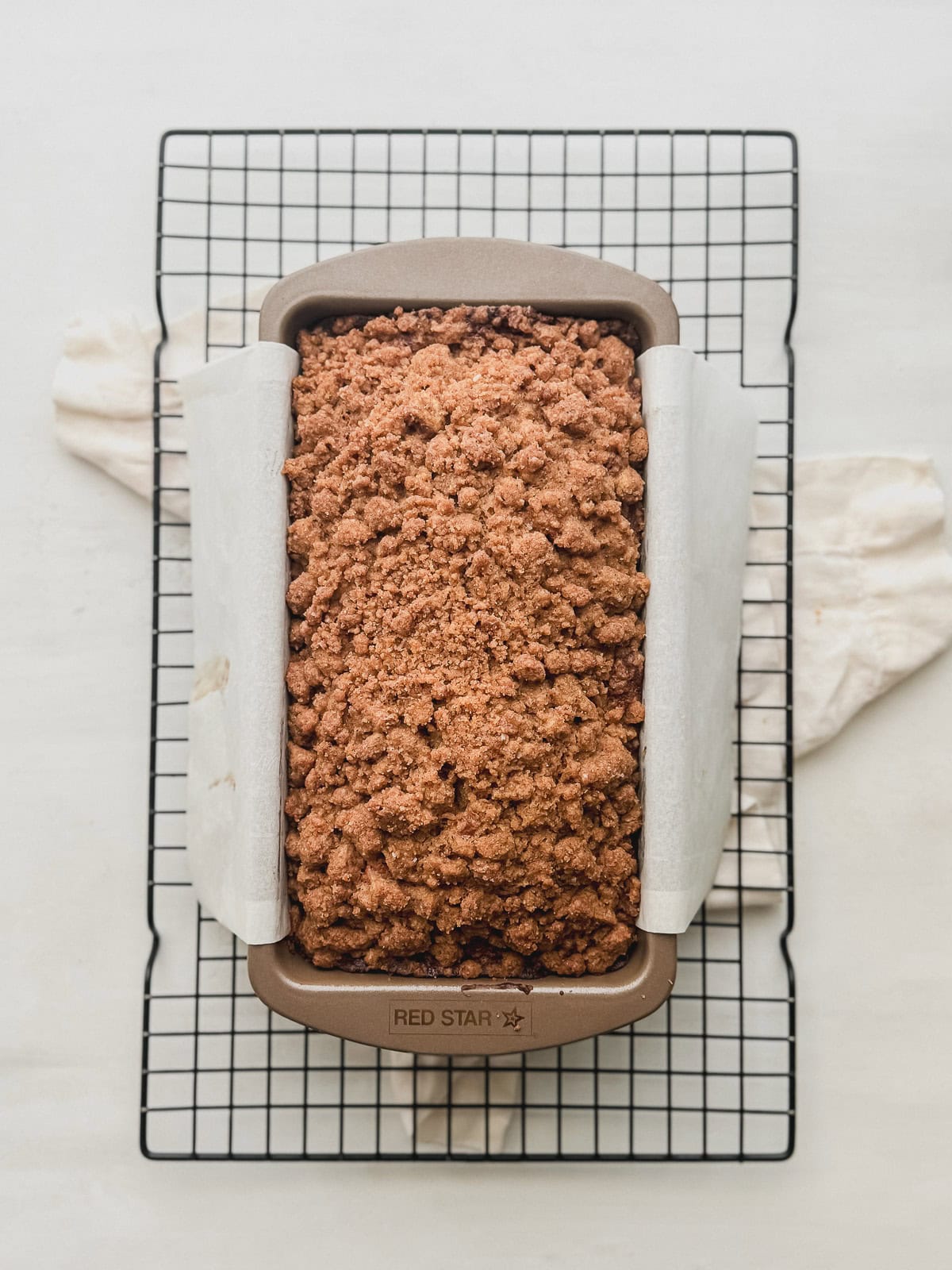 Baked banana bread with streusel topping in a loaf pan on a cooling rack.