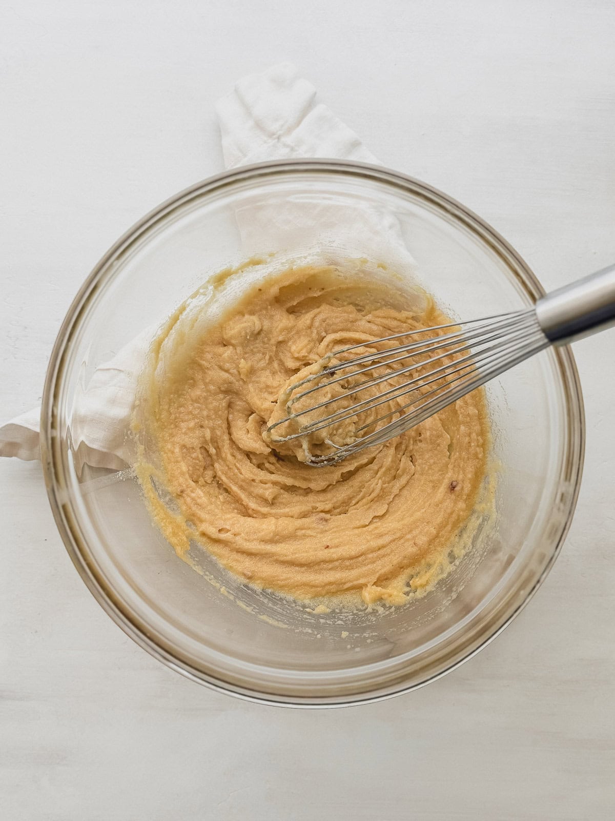 Butter and sugars whisked together in a glass bowl with a whisk.