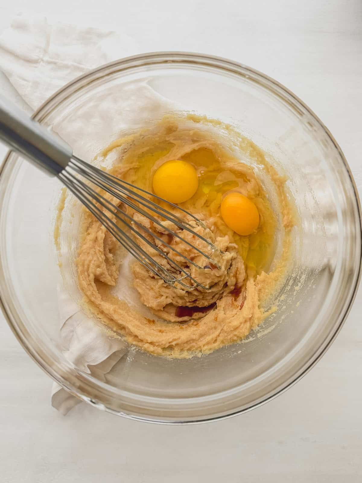 Eggs and vanilla extract added to butter mixture in a glass bowl with a whisk.