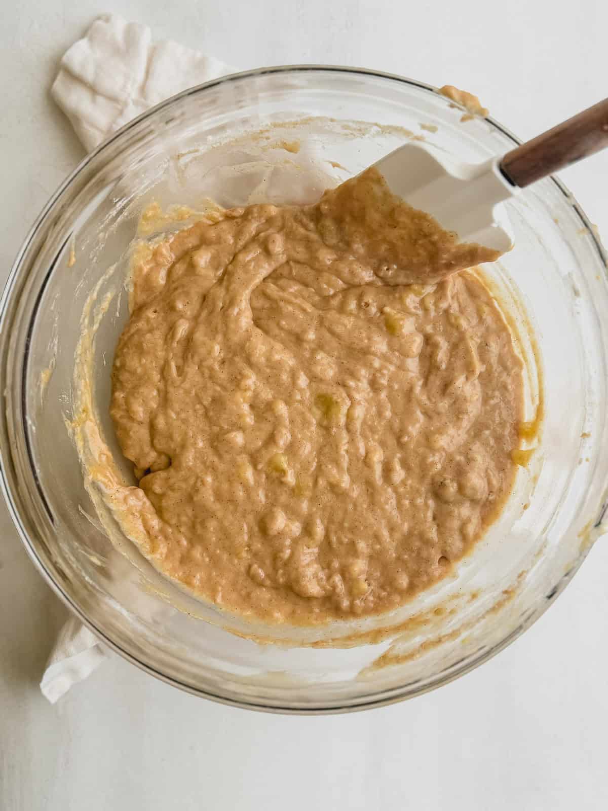 Banana bread batter in a glass bowl with a rubber spatula.