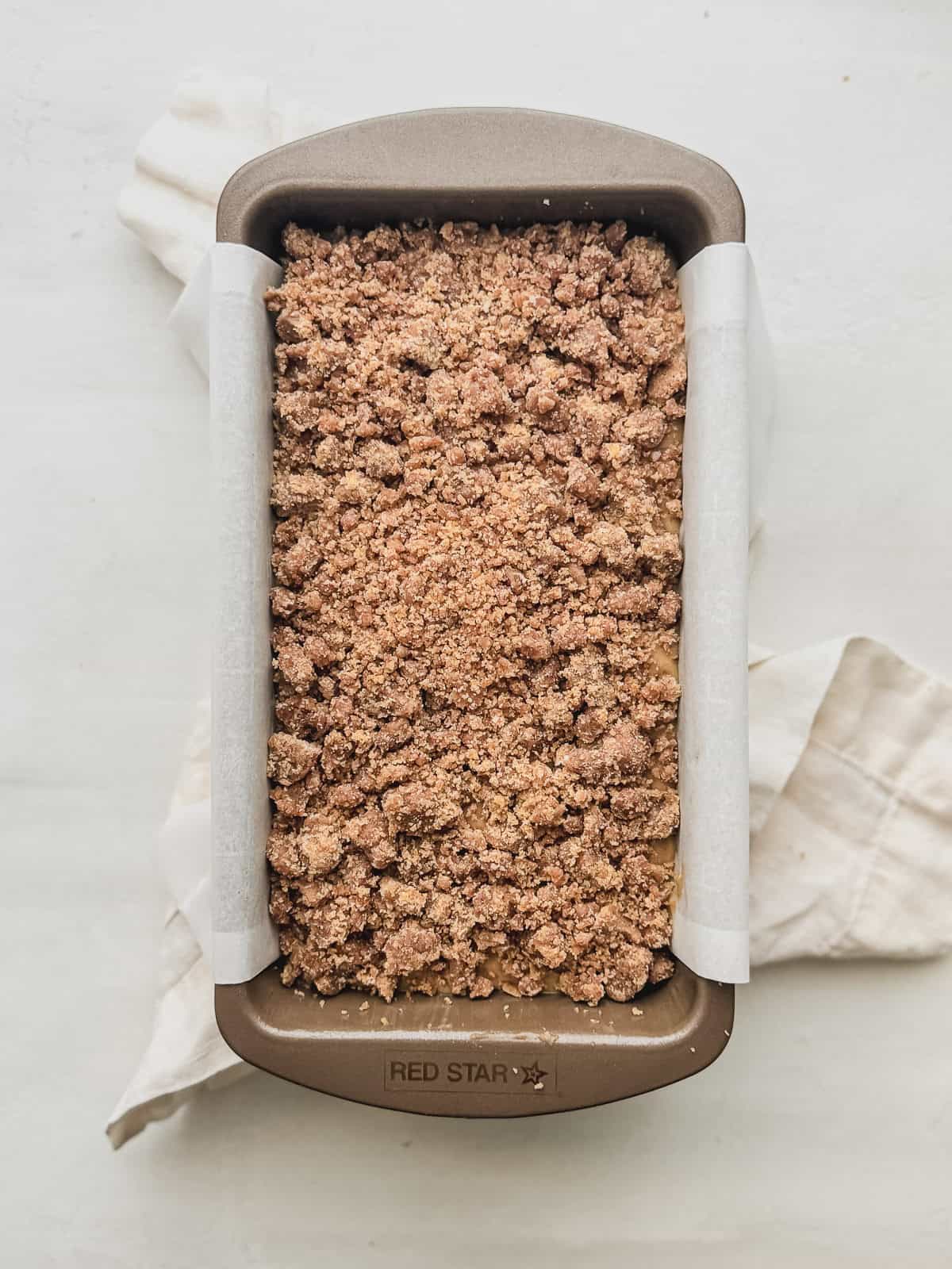 Banana bread batter in a loaf pan lined with parchment topped with streusel.