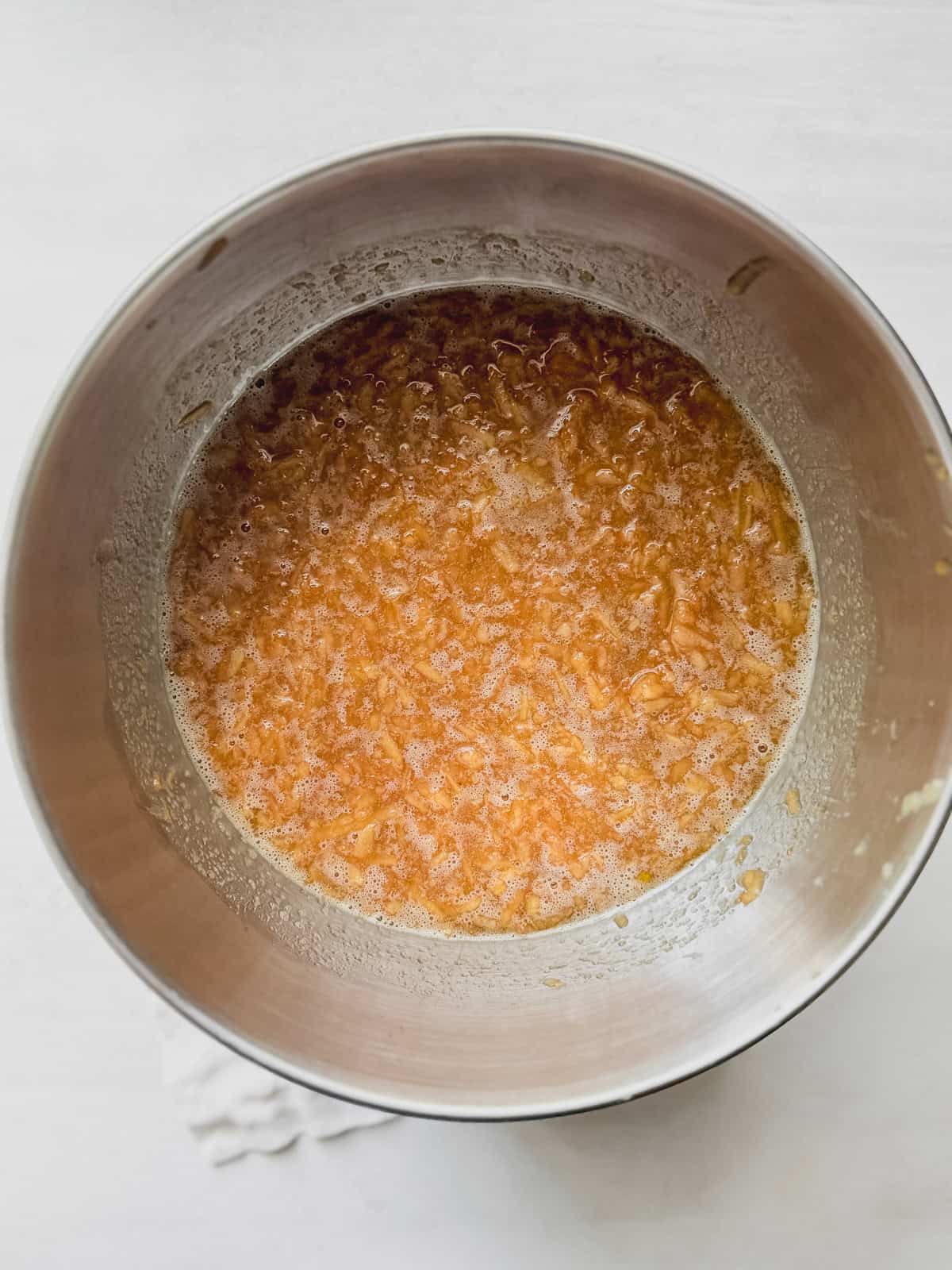 A mixing bowl with cream wet ingredients and shredded apples.