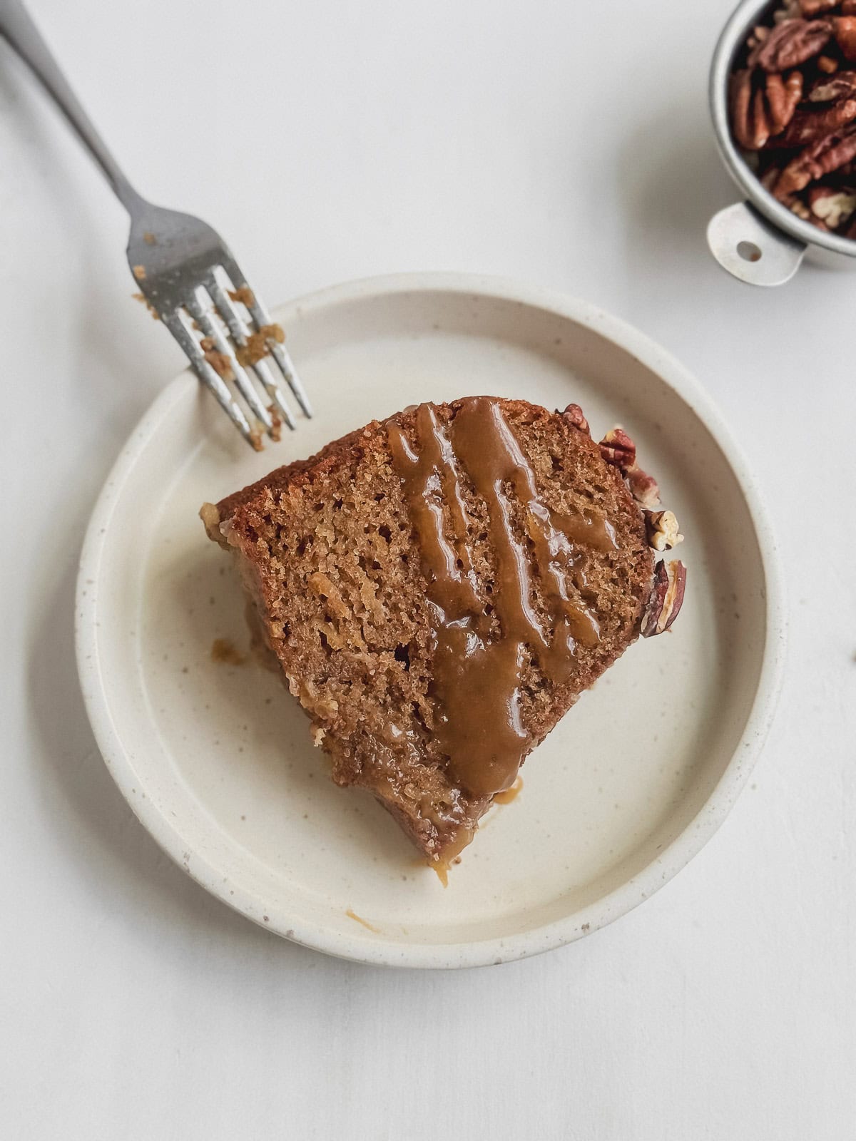 A slice of apple pecan cake on a plate with caramel drizzled on top.